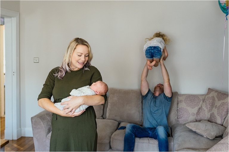 mum-holding-newborn-daughter-dad-throwing-oldest-daughter-into-air-in-background