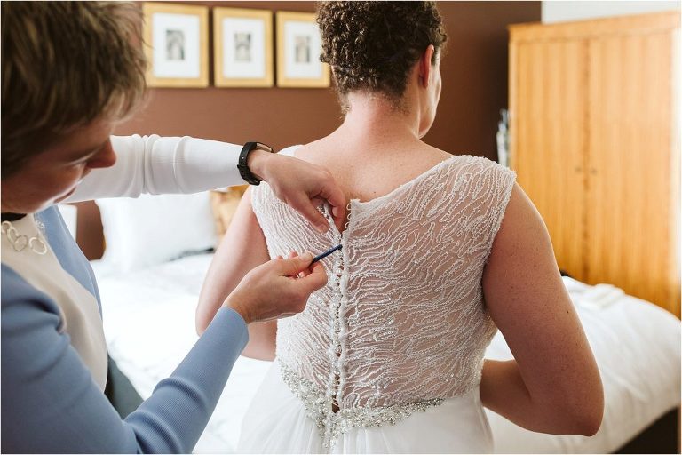 friend-using-crochet-hook-to-do-buttons-up-on-wedding-dress