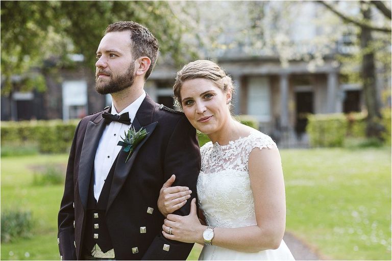 bride-holds-on-to-grooms-arm-and-looks-towards-camera