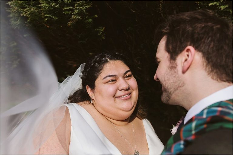 bride-looking-at-groom-while-veil-blows-in-the-wind