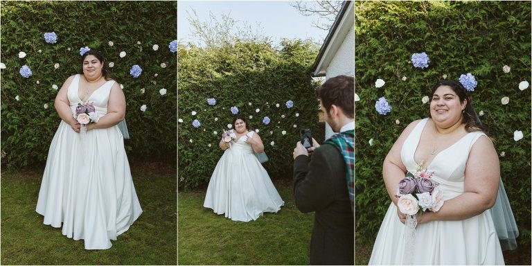 bride-poses-with-hedge-backdrop-and-groom-takes-a-photo-on-his-phone