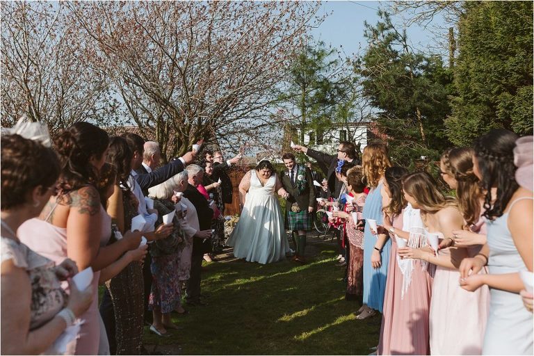 bride-and-groom-walk-through-confetti-tunnel-with-wedding-guests-either-side