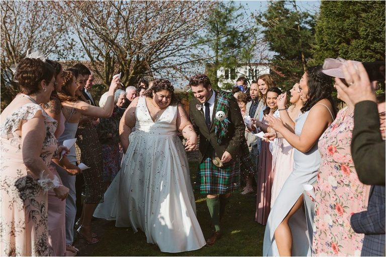 guests-throw-confetti-over-bride-and-groom-as-they-walk-through-confetti-tunnel