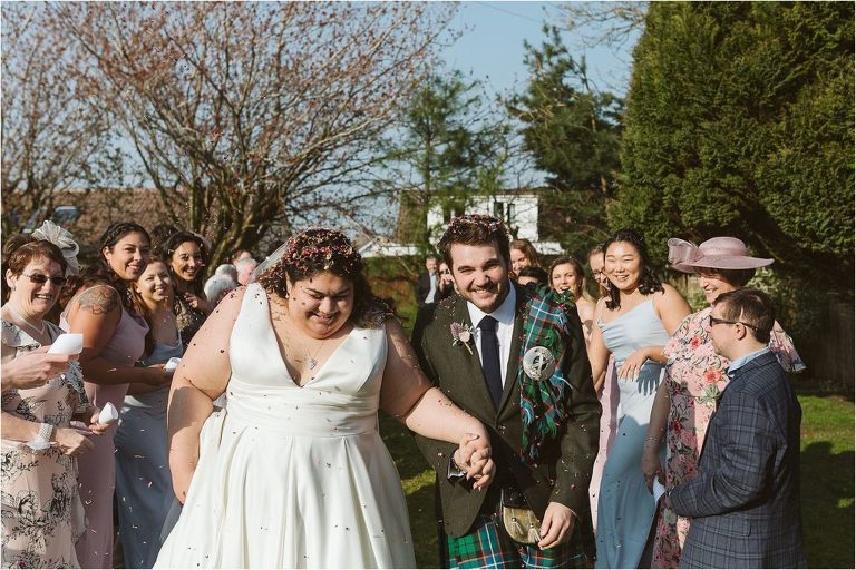 bride-and-groom-emerge-from-confetti-tunnel-covered-in-confetti