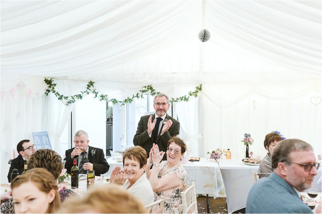 grooms-dad-stands-and-claps-while-bride-and-groom-cut-cake