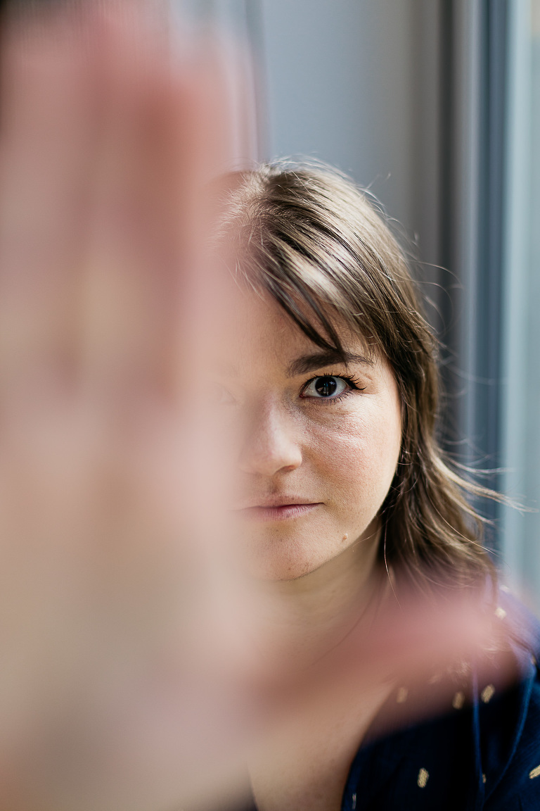 woman-looking-in-to-camera-covering-half-of-camera-with-hand