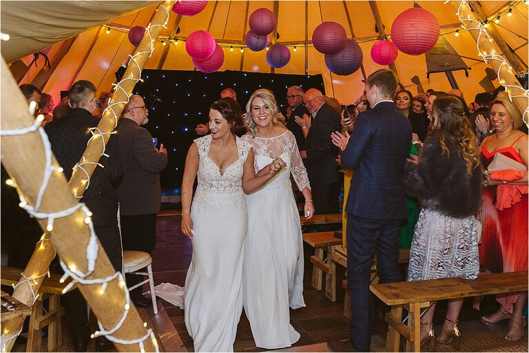 brides-walk-out-as-wife-and-wife-holding-hands-smiling-at-guests