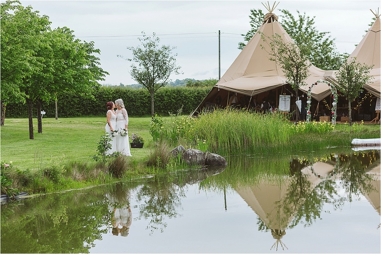 brides-kissing-beside-pond-tipi-in-background