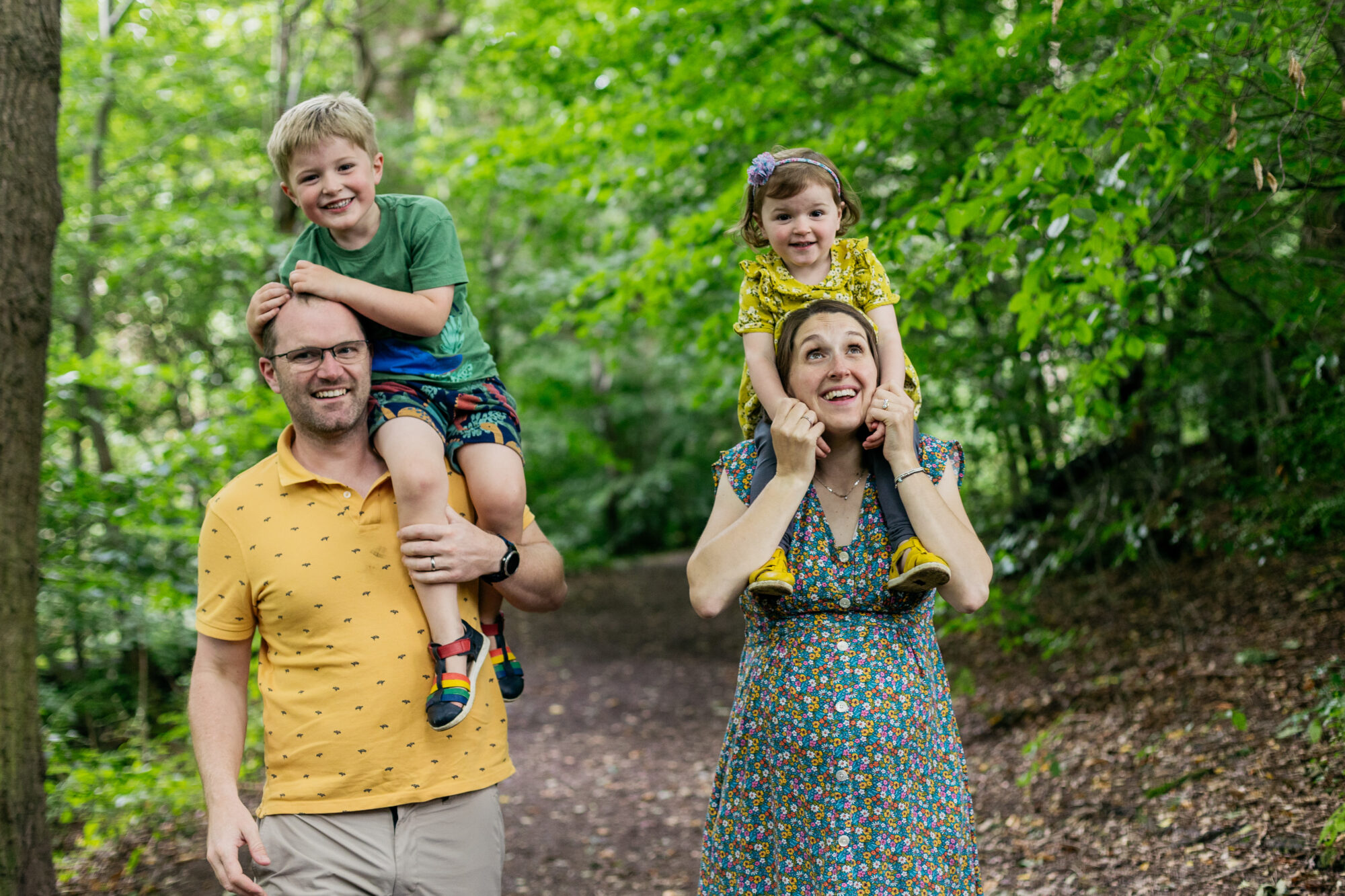 son-is-on-dads-shoulders-looking-at-camera-daughter-is-on-mums-shoulders-as-mum-looks-up-at-her