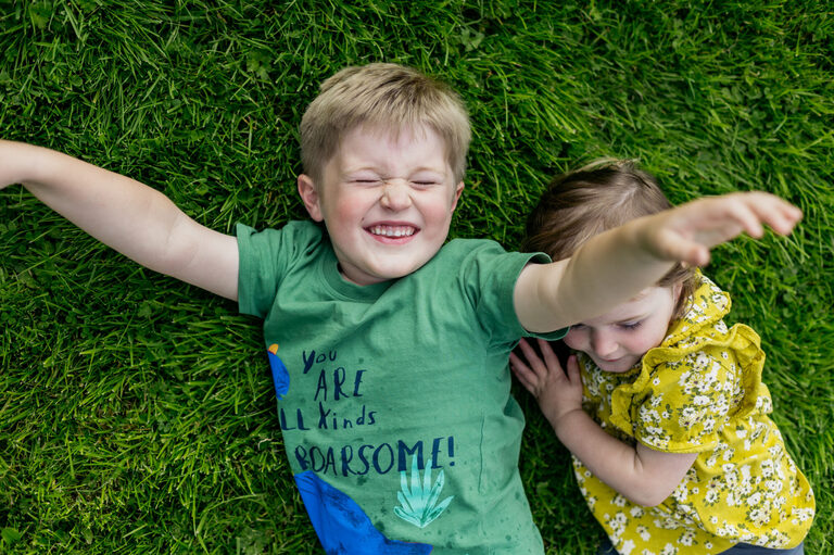 boy-iis-lying-on-grass-with-sister-beside-him-his-eyes-are-closed-as-he-smiles