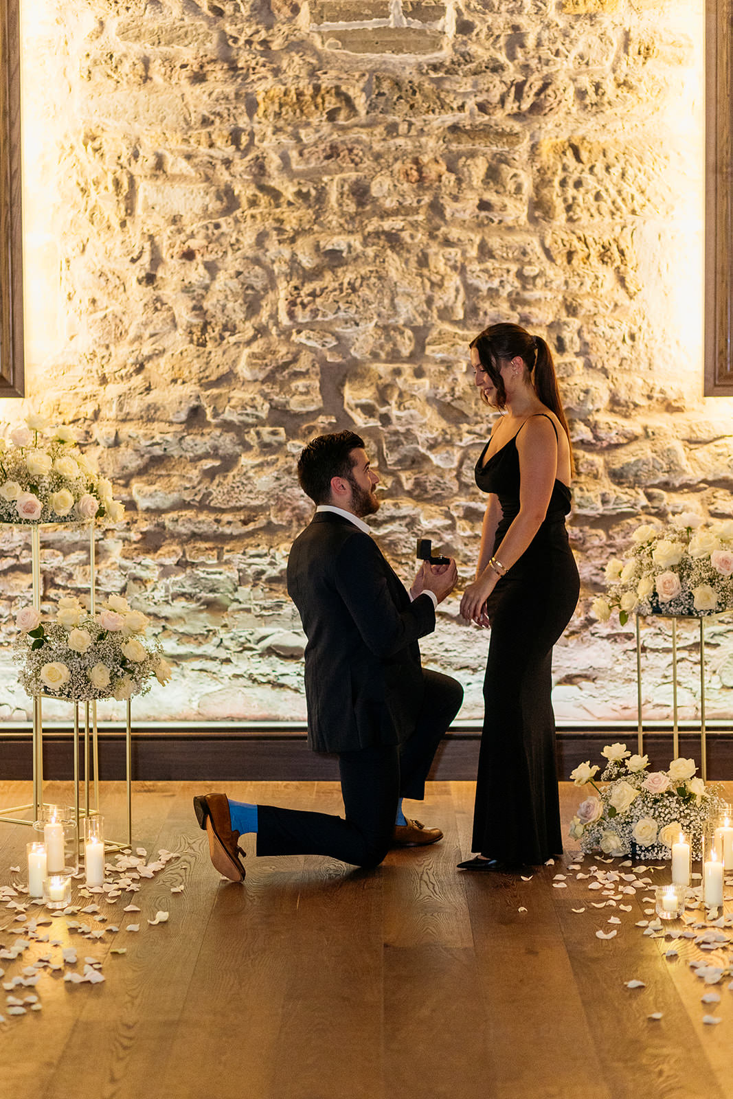 man-is-on-bended-knee-asking-his-girlfriend-to-marry-him-they-are-surrounded-by-bouquets-of-white-and-pink-roses