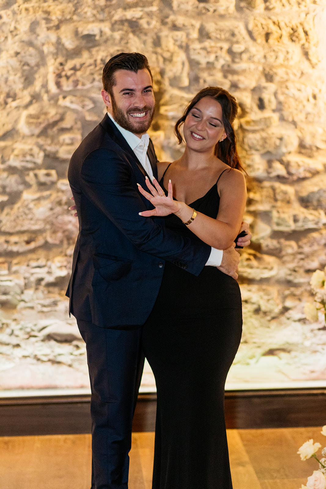 woman-looking-at-her-new-engagement-ring-as-her-fiancee-looks-towards-camera-smiling