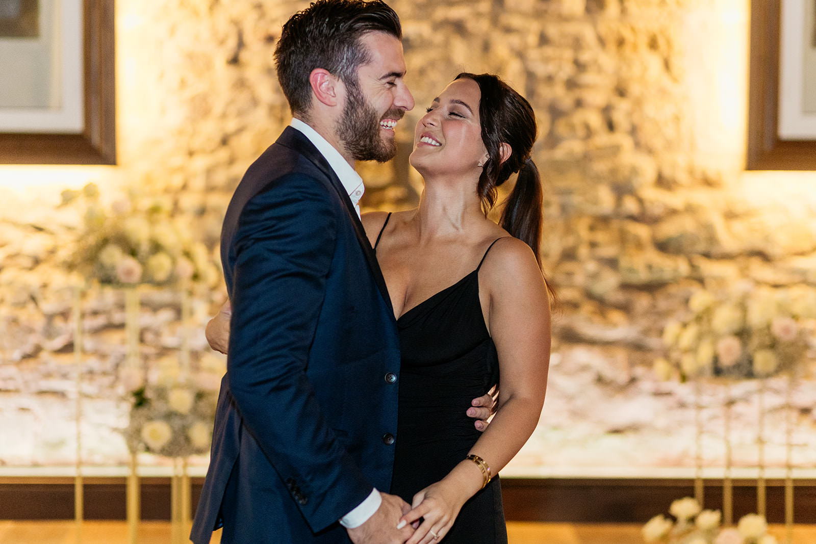 woman-looking-at-her-fiance-laughing-and-smiling-white-and-pink-roses-on-pedestal-in-background
