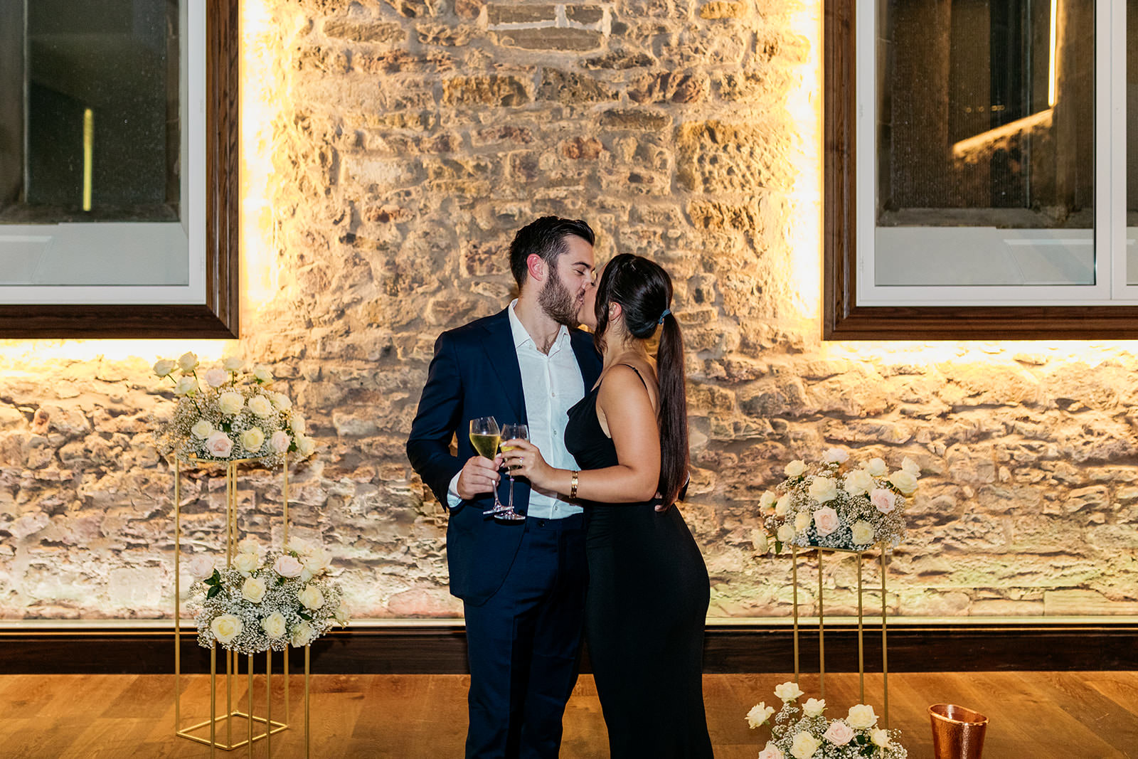 couple-kiss-they-are-surrounded-by-pink-and-white-roses-on-pedestals-as-they-have-just-got-engaged