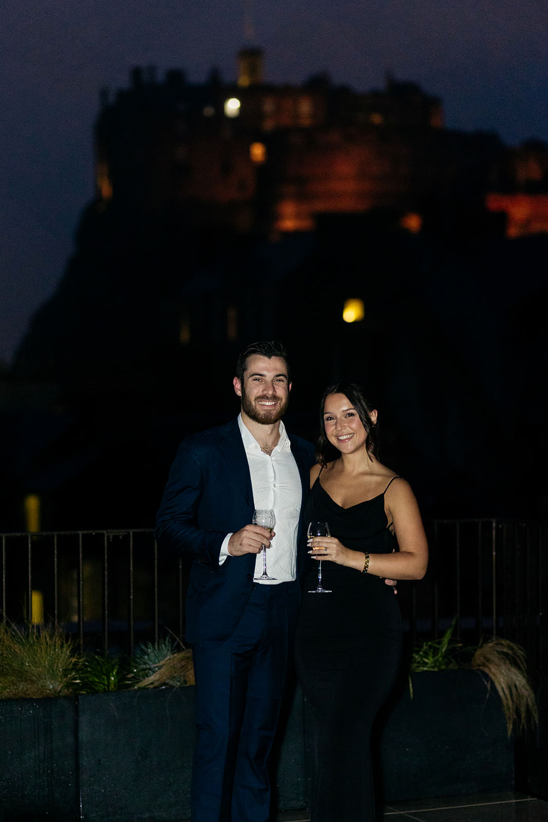 newly-engaged-couple-pose-on-the-rooftop-of-the-virgin-hotel-in-Edinburgh-castle-in-the-background