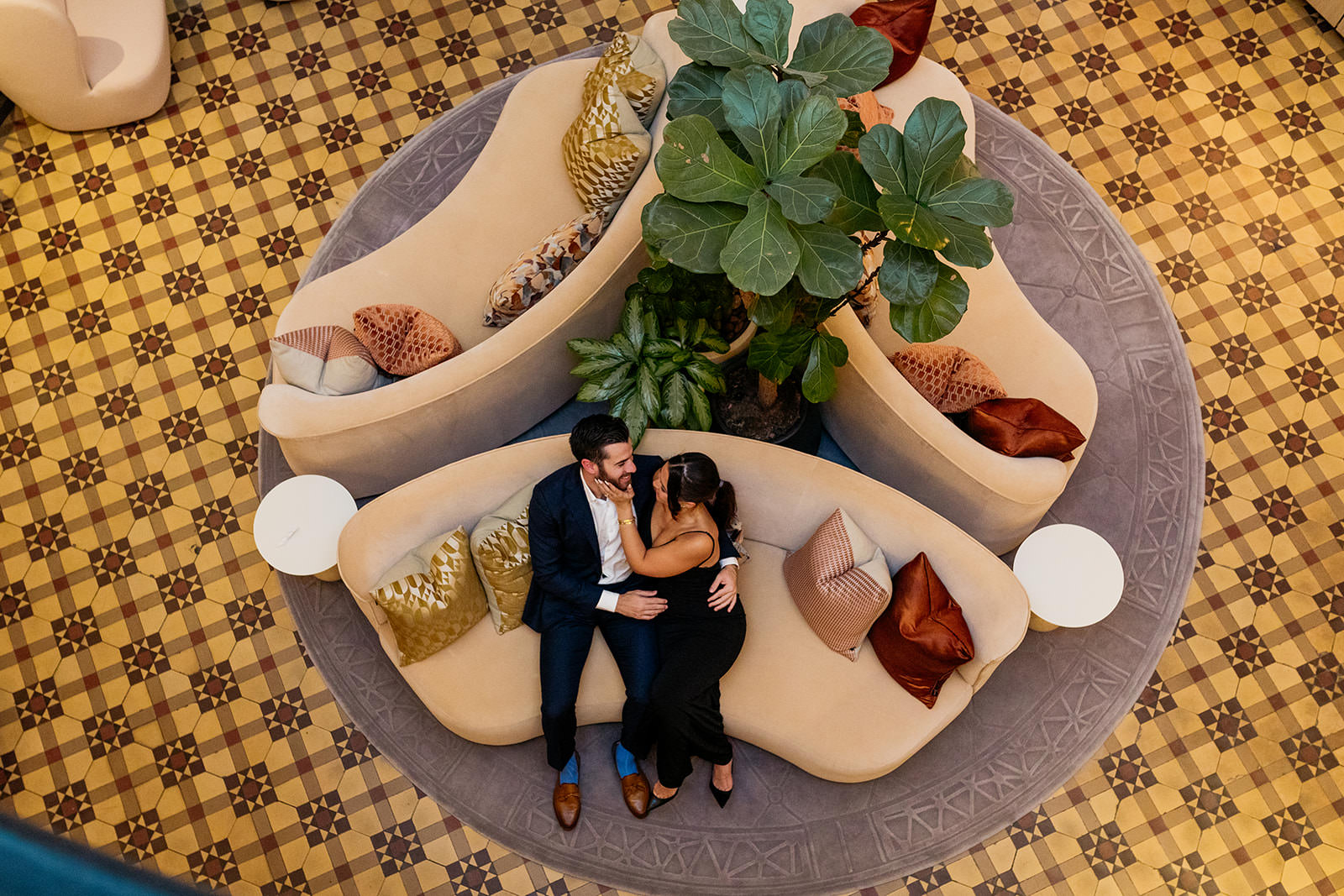 couple-sit-on-the-sofa-we-are-looking-down-on-them-from-up-high-they-are-holding-each-other-and-the-woman-is-touching-her-fiances-face