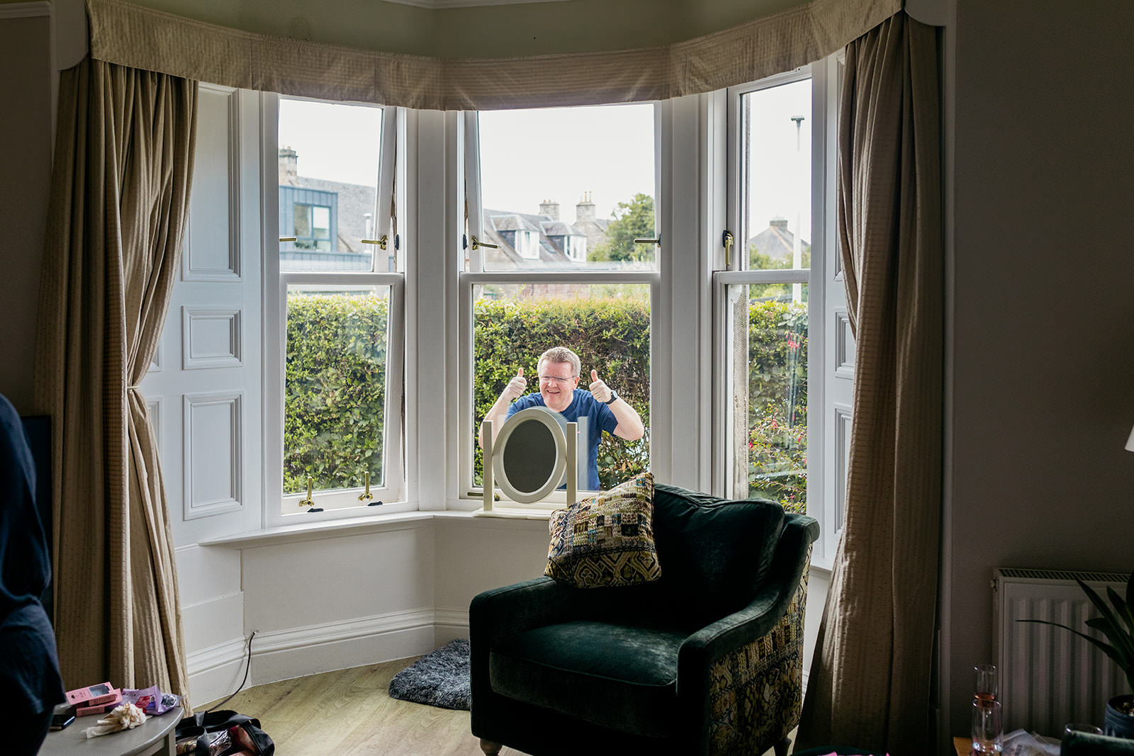a man is outside the living room window looking inwards. He is giving two thumbs up and smiling.