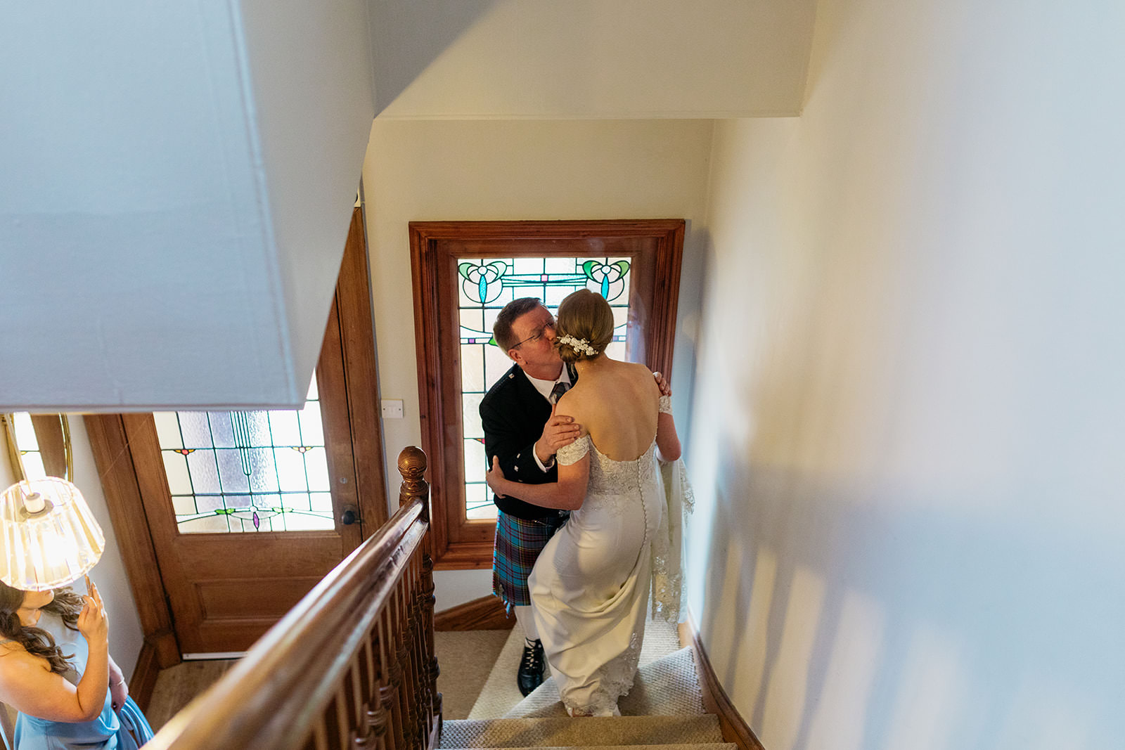 the brides father is kisses his daughter on the cheek as they meet at the bottom of the stairs.