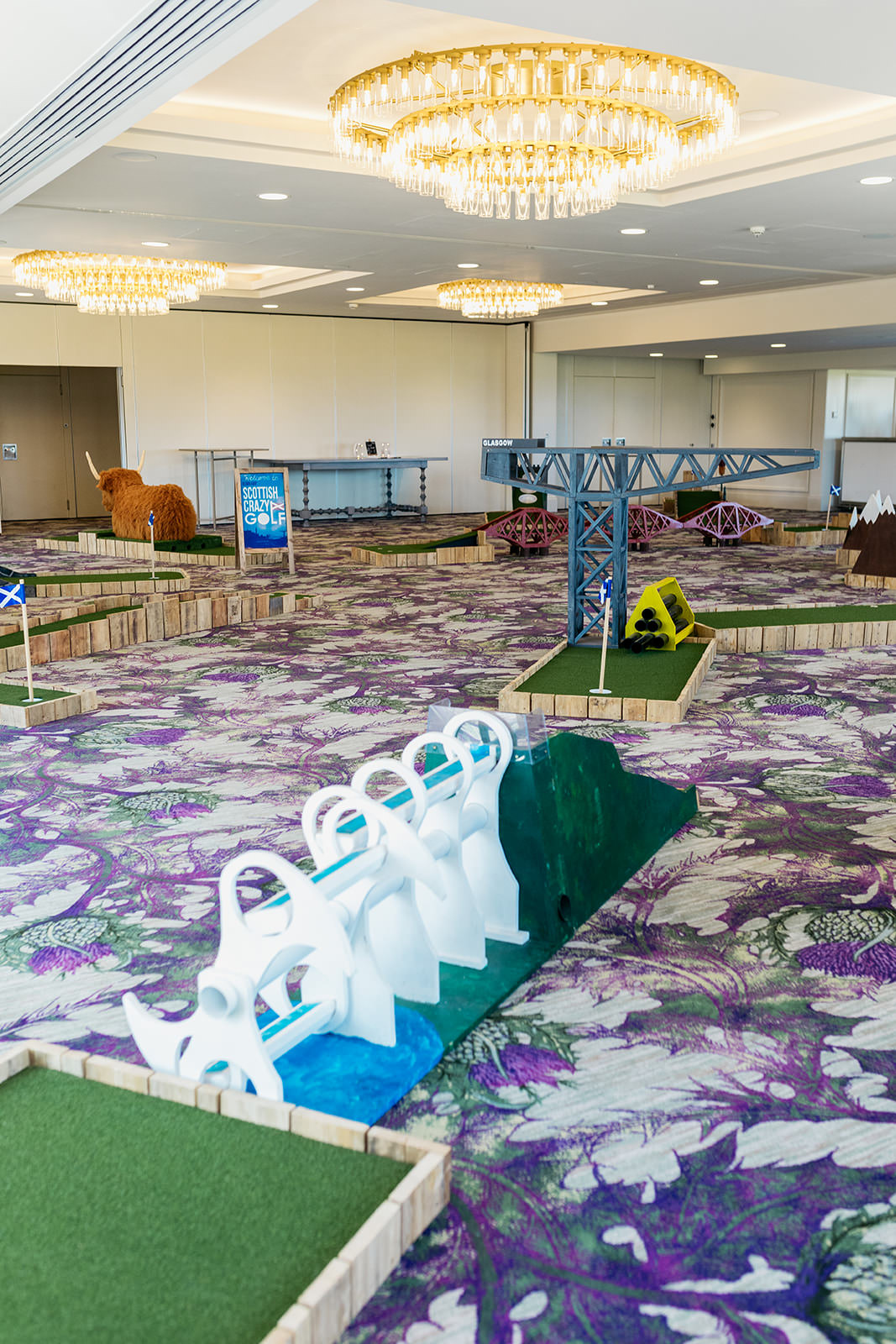 a room is set up with Scottish crazy golf. each hole has a Scottish theme like the Falkirk wheel, Glasgow crane Forth rail bridge and a Highland cow.