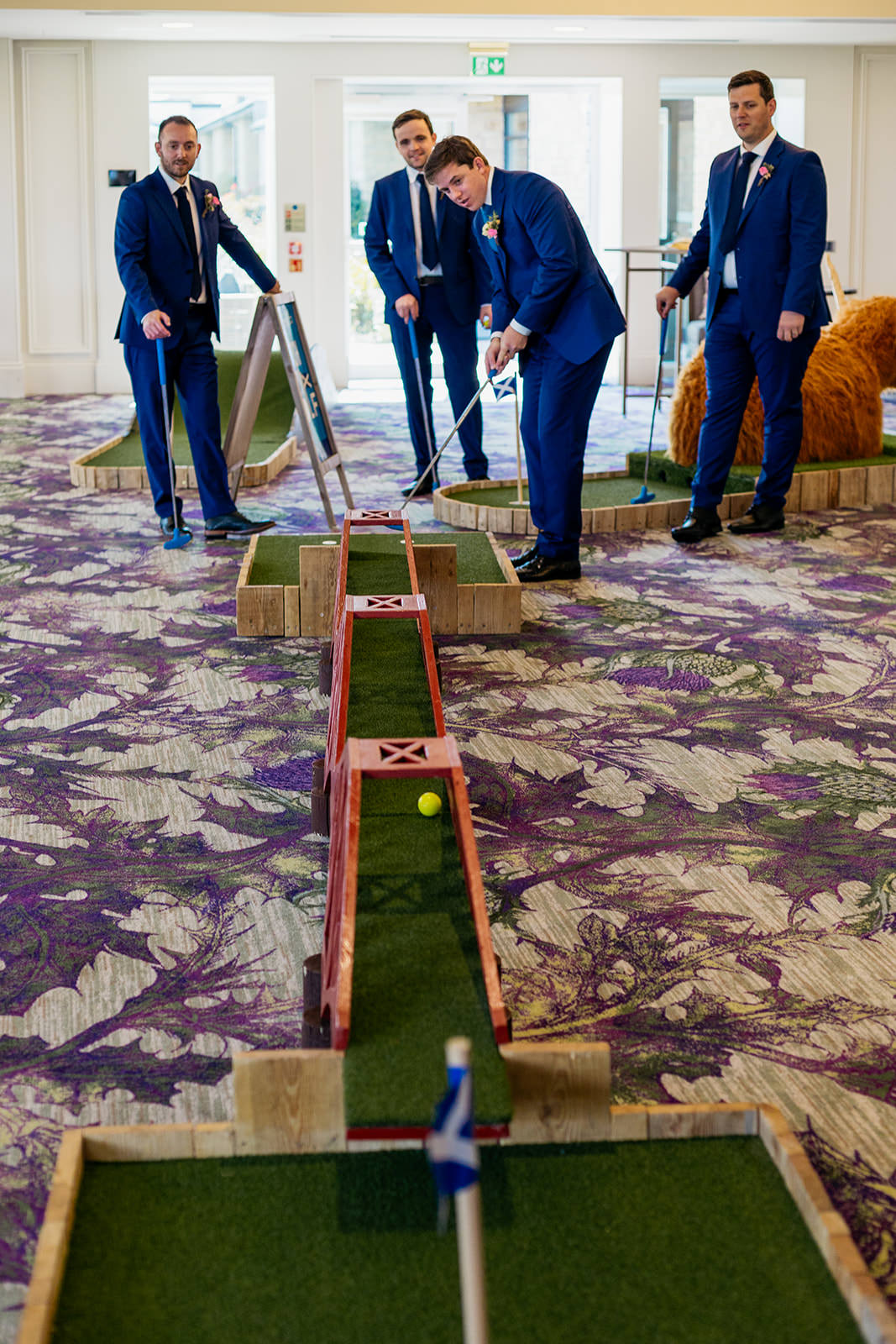 Groomsmen are playing crazy golf, and the yellow ball half way down down the ramp.