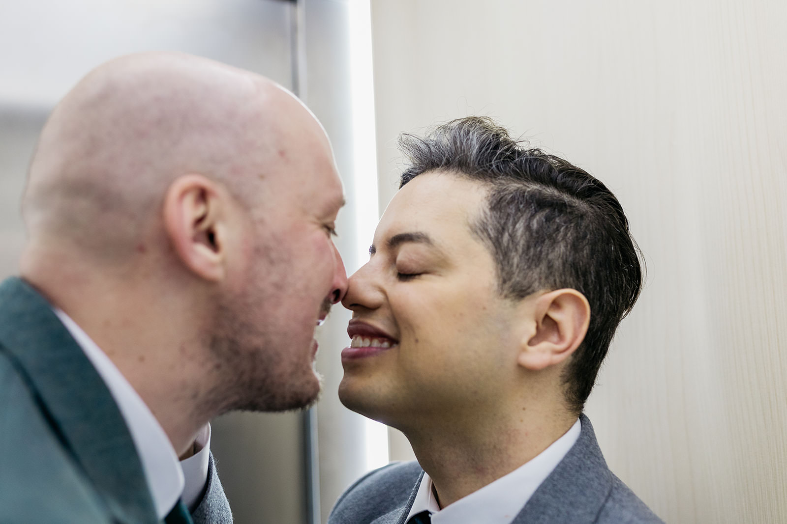 a man is touching noses with his husband. their eyes are closed and they are smiling.