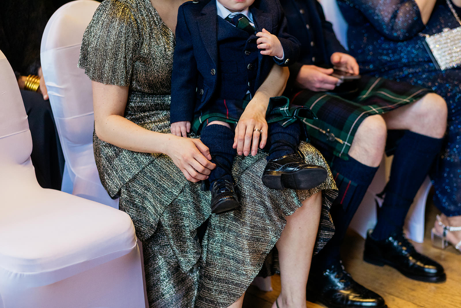 a child is sitting on his mum's knee and she is adjusting his kilt socks