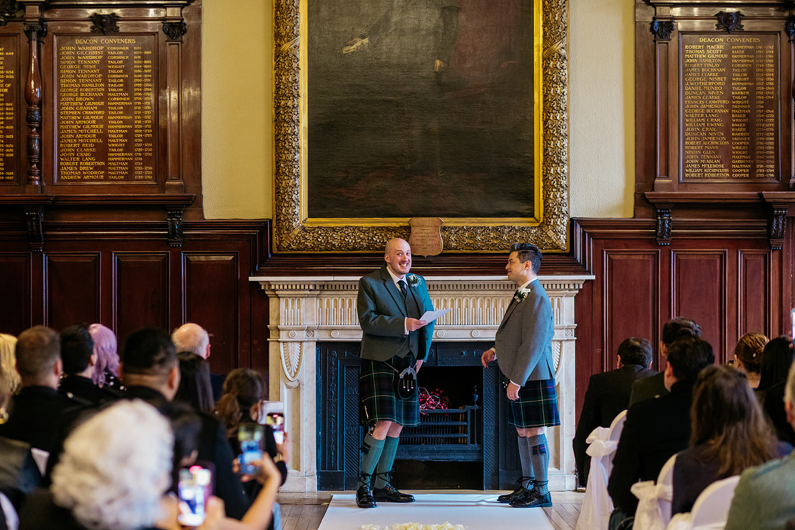two grooms are standing and one groom is reading from a piece of paper and smiling.