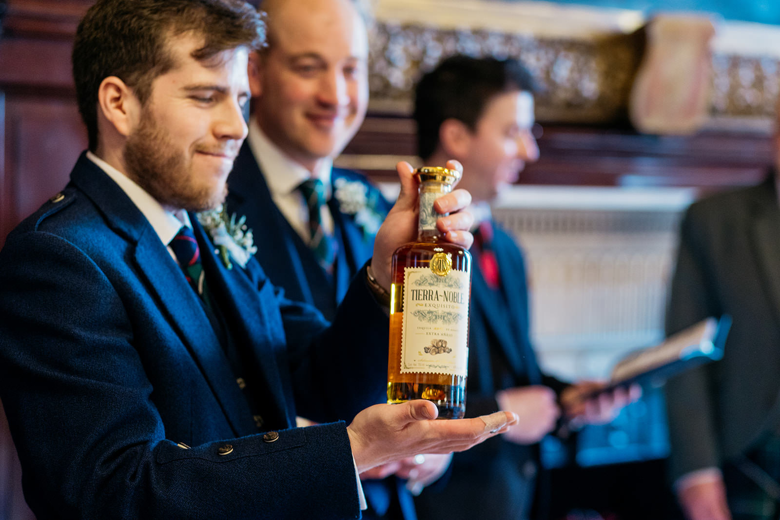a groomsman at a wedding is holding a bottle of tierra-noble in his hands.