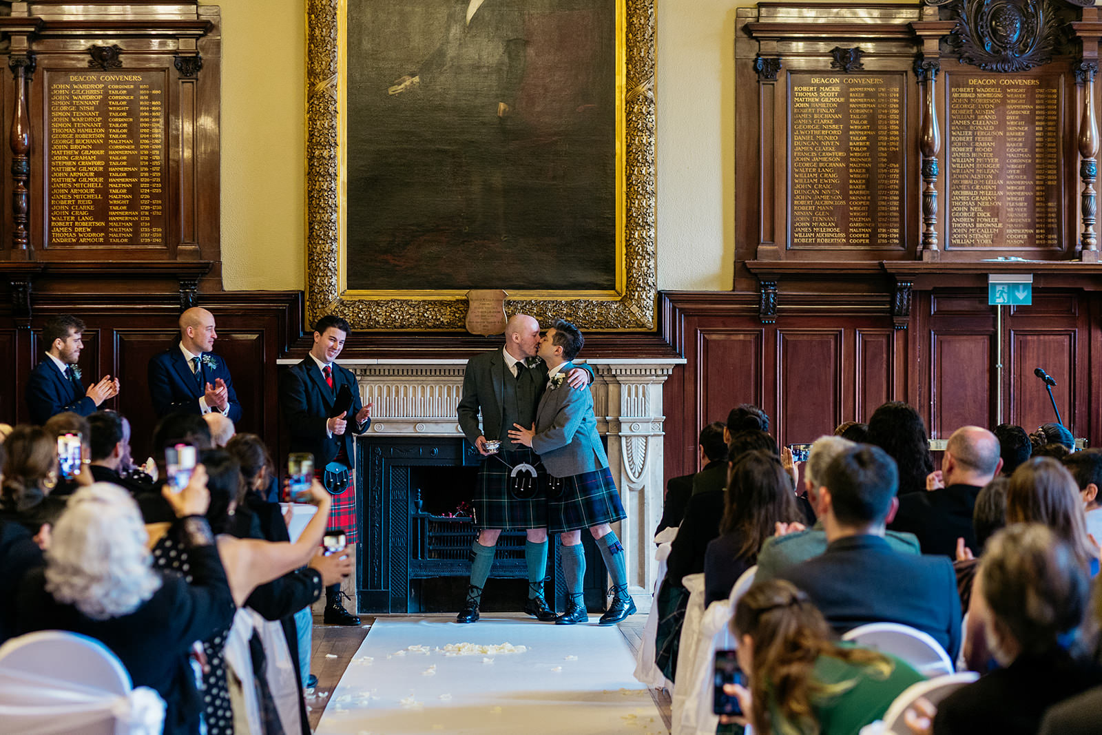 two grooms are sharing their first kiss as a married couple. the guests are clapping and cheering from them