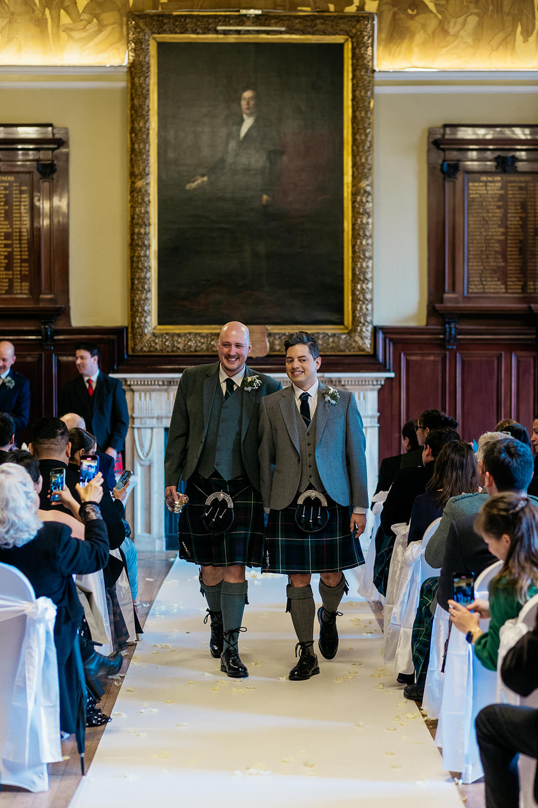 two grooms are walking down the aisle at the end of their wedding ceremony at Trades Hall in Glasgow.