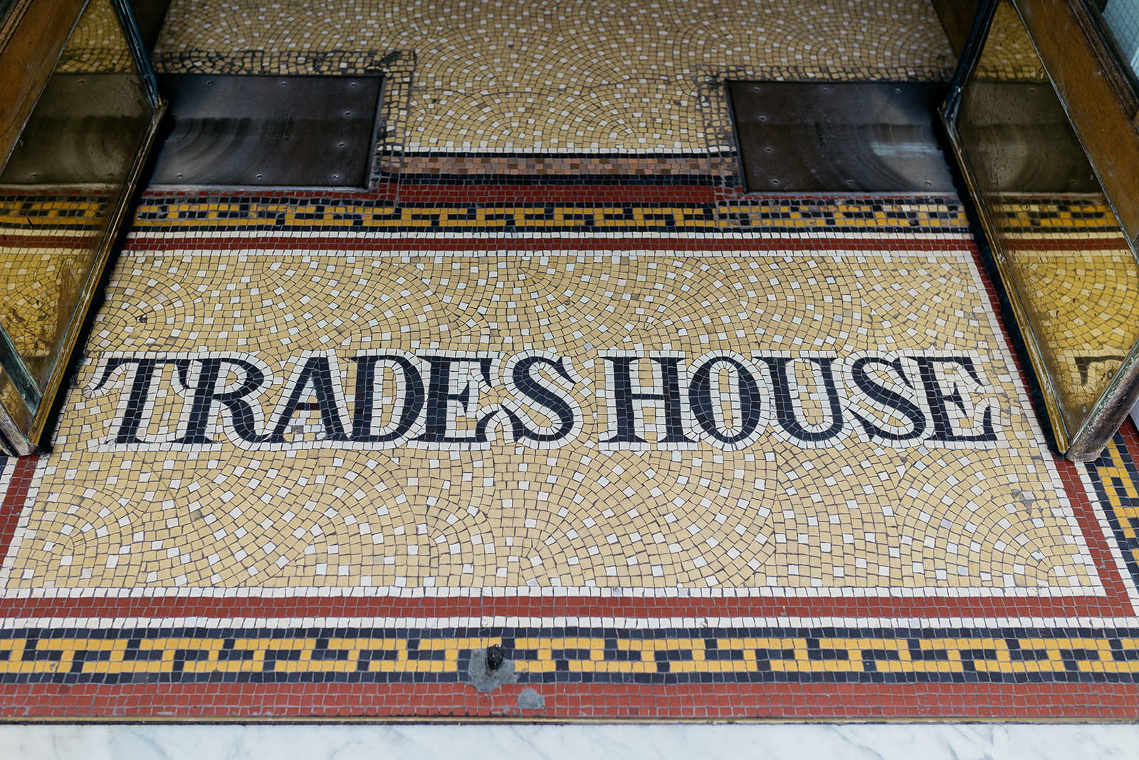 mosaic tiles are on the floor and it spells out trades house.