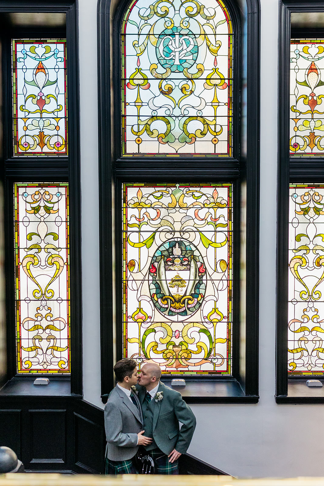 a gay couple are standing underneath the stained glass in the staircase of the AC hotel. they are sharing a kiss.