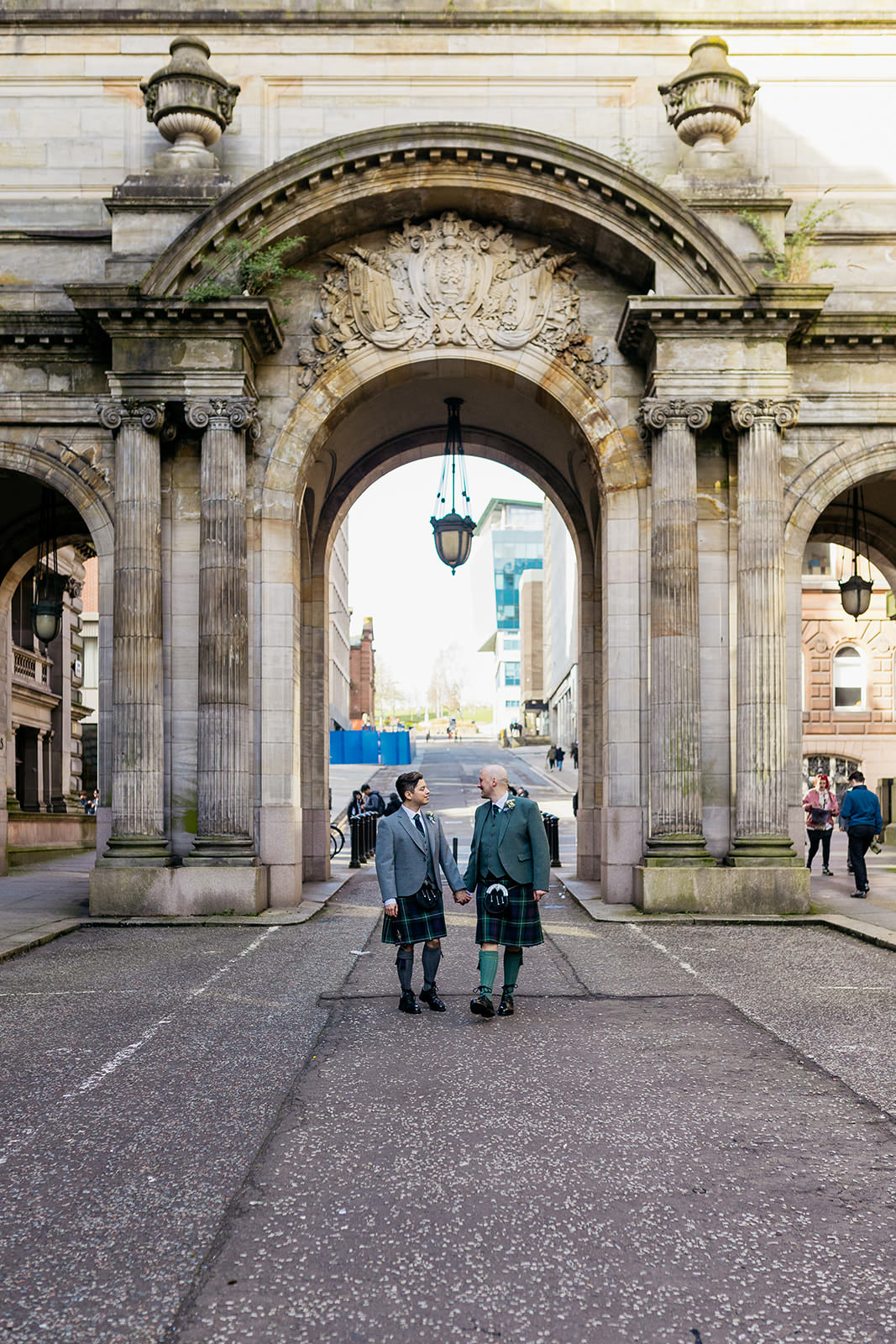 a couple are walking in the city centre of Glasgow. They are framed by the arches on John Street.