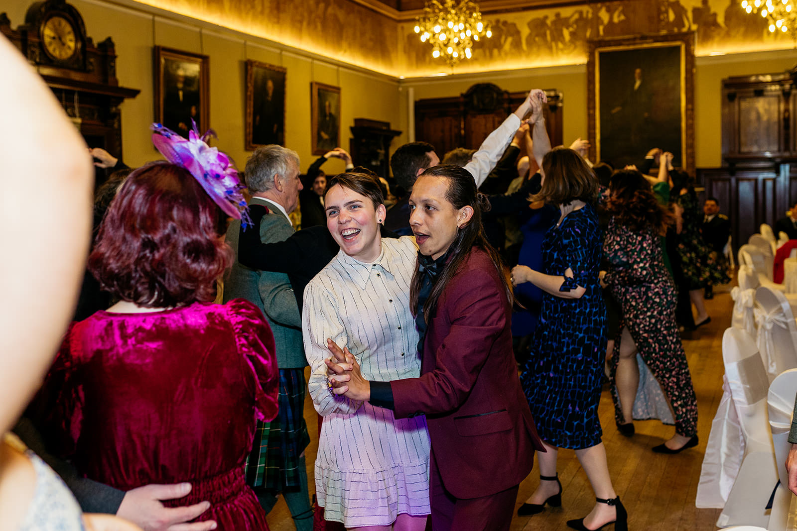 guests are ceilidh dancing at a wedding at the Trades Hall. They are laughing and holding each other in a ballroom pose.