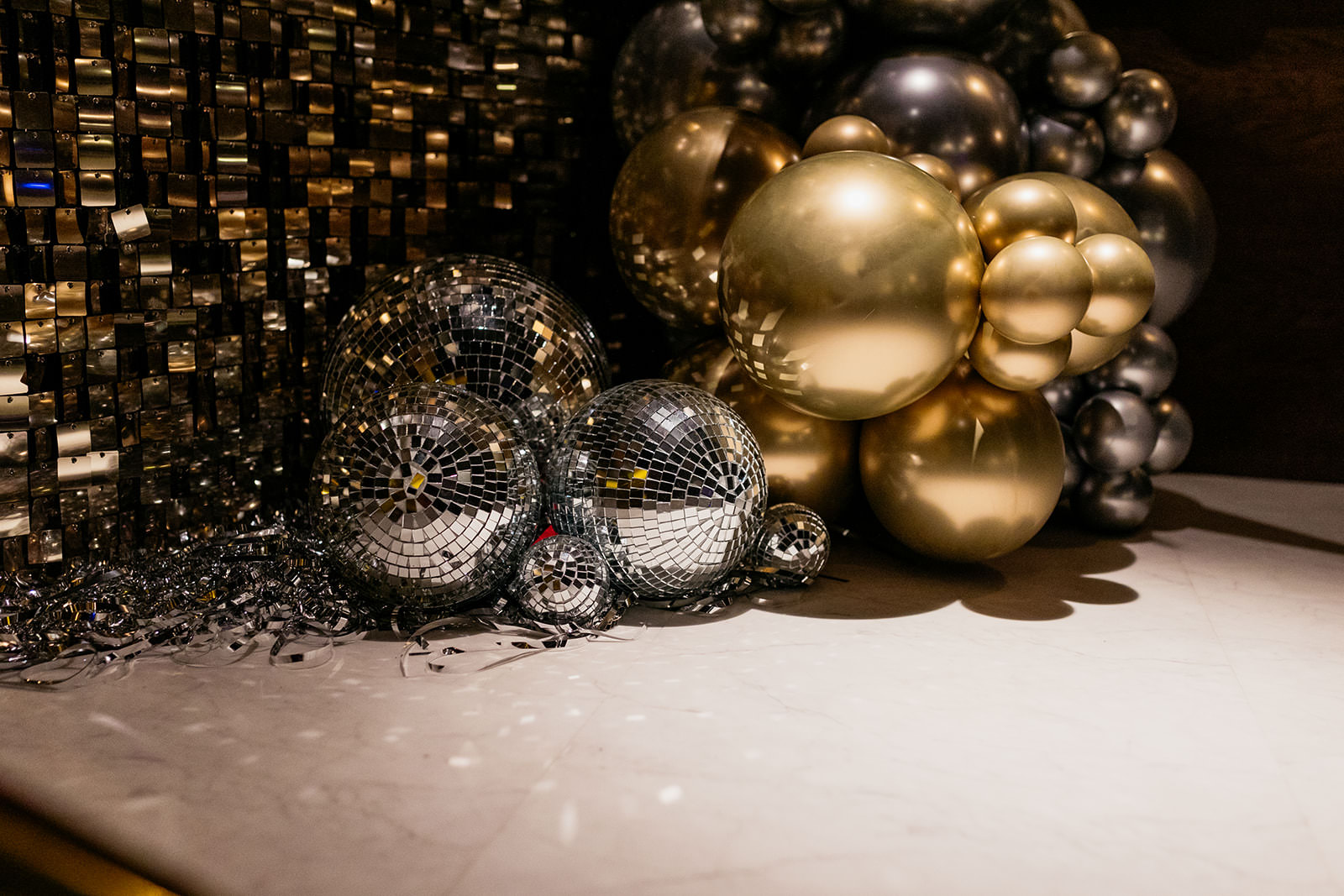 a collection of mirrorballs and gold balloons are place in front of a glittery backdrop