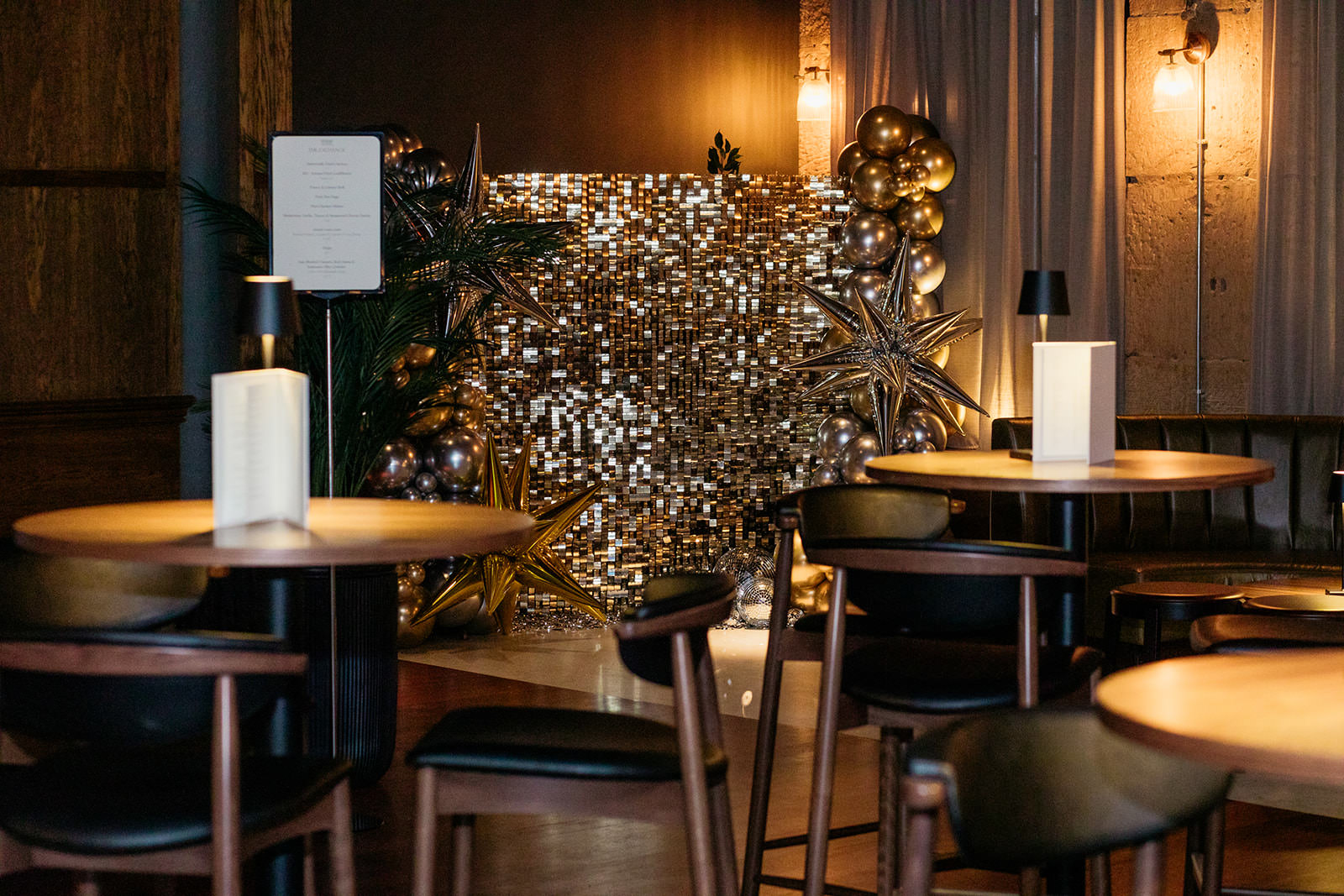 the is a gold glittery backdrop set up in an events room with star balloons.