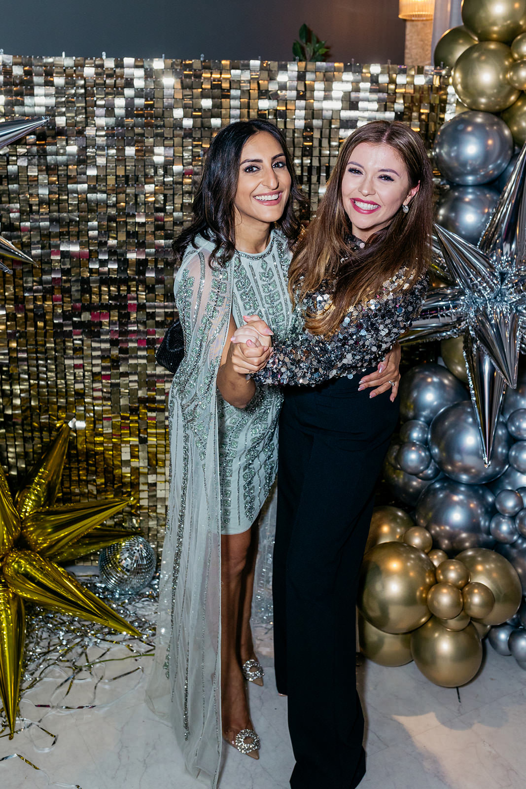 Dr. Punam and radio presenter Amber Zoe are standing in a ballroom pose smiling. they are in front of a gold glittery backdrop and there are gold and silver balloons at either side of them.