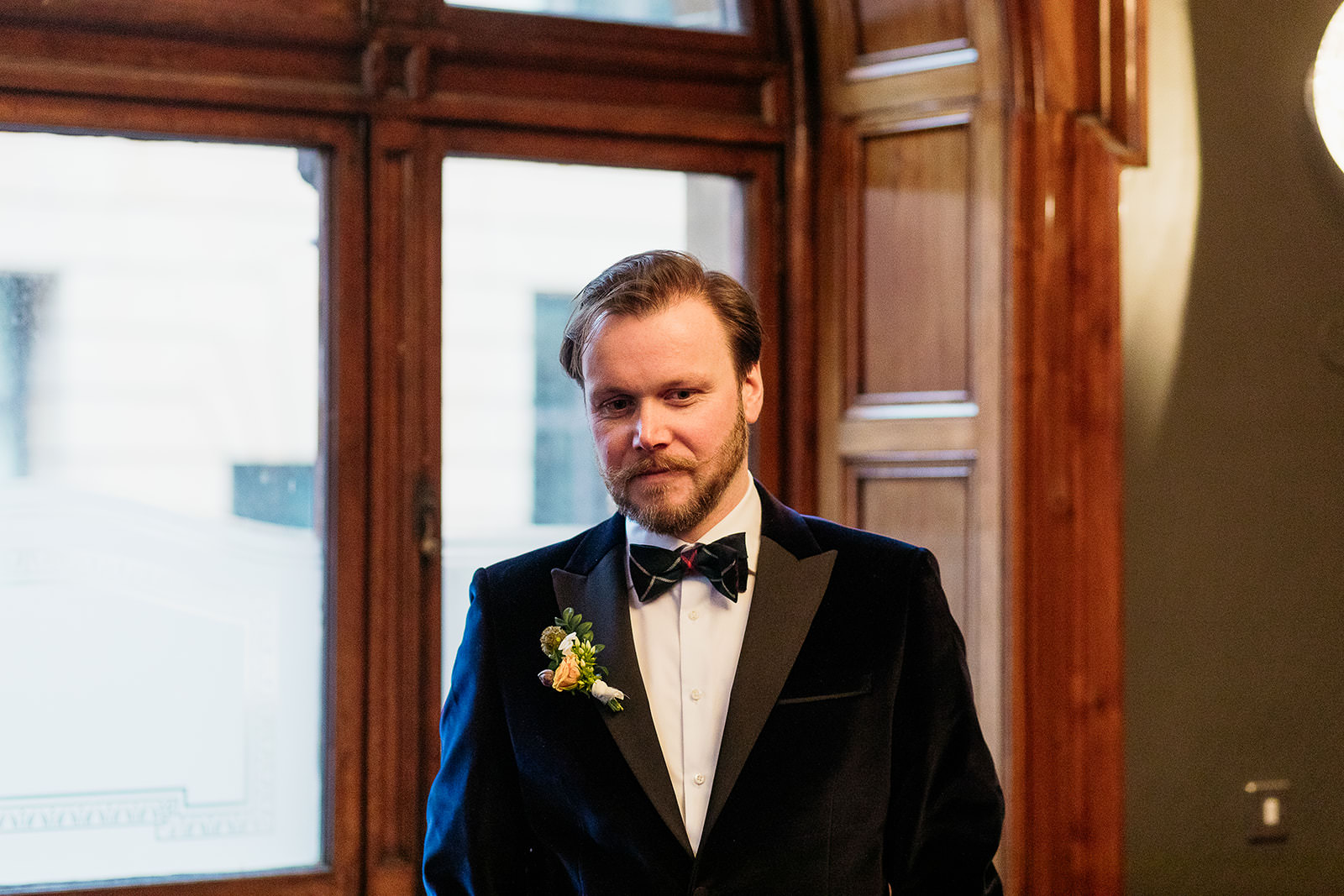 groom is waiting inside montrose street registry office. he is wearing a dark blue velvet jacket with a white shirt and tartan bow tie.