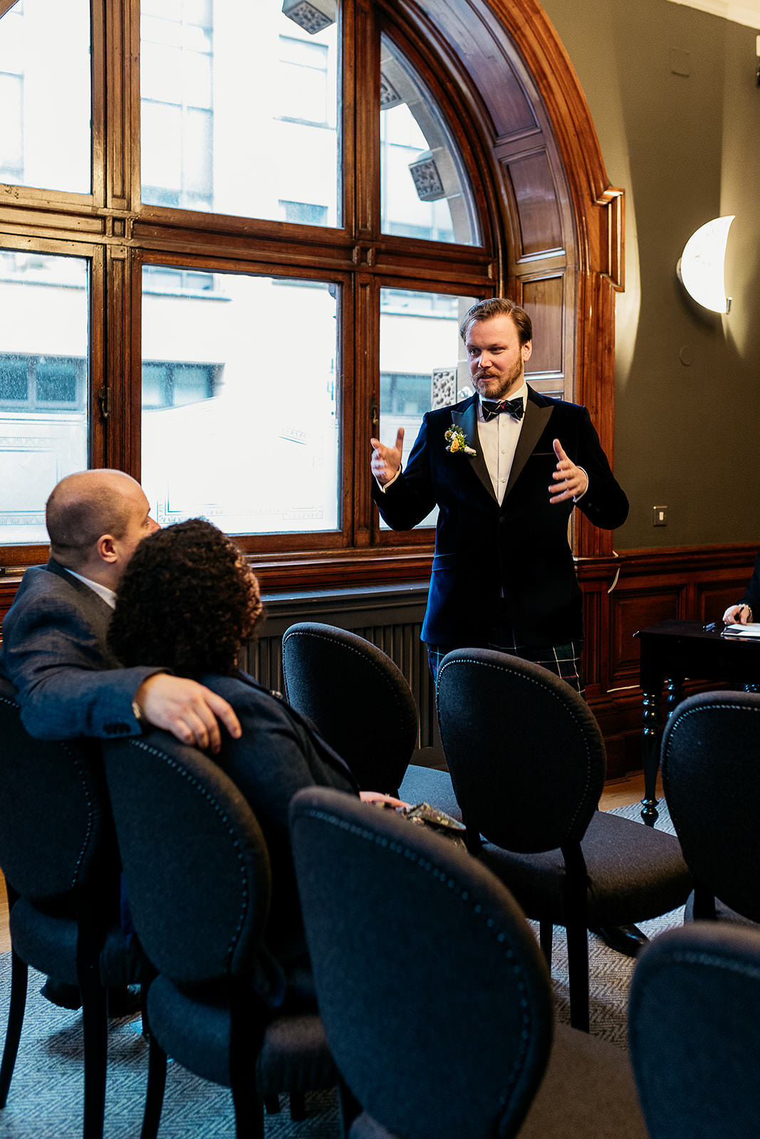 a man is standing talking to his friends who are seated. He is gesturing with his hands.
