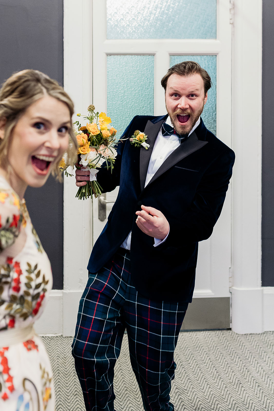 a groom is holding the bridal bouquet and pointing towards the bride.