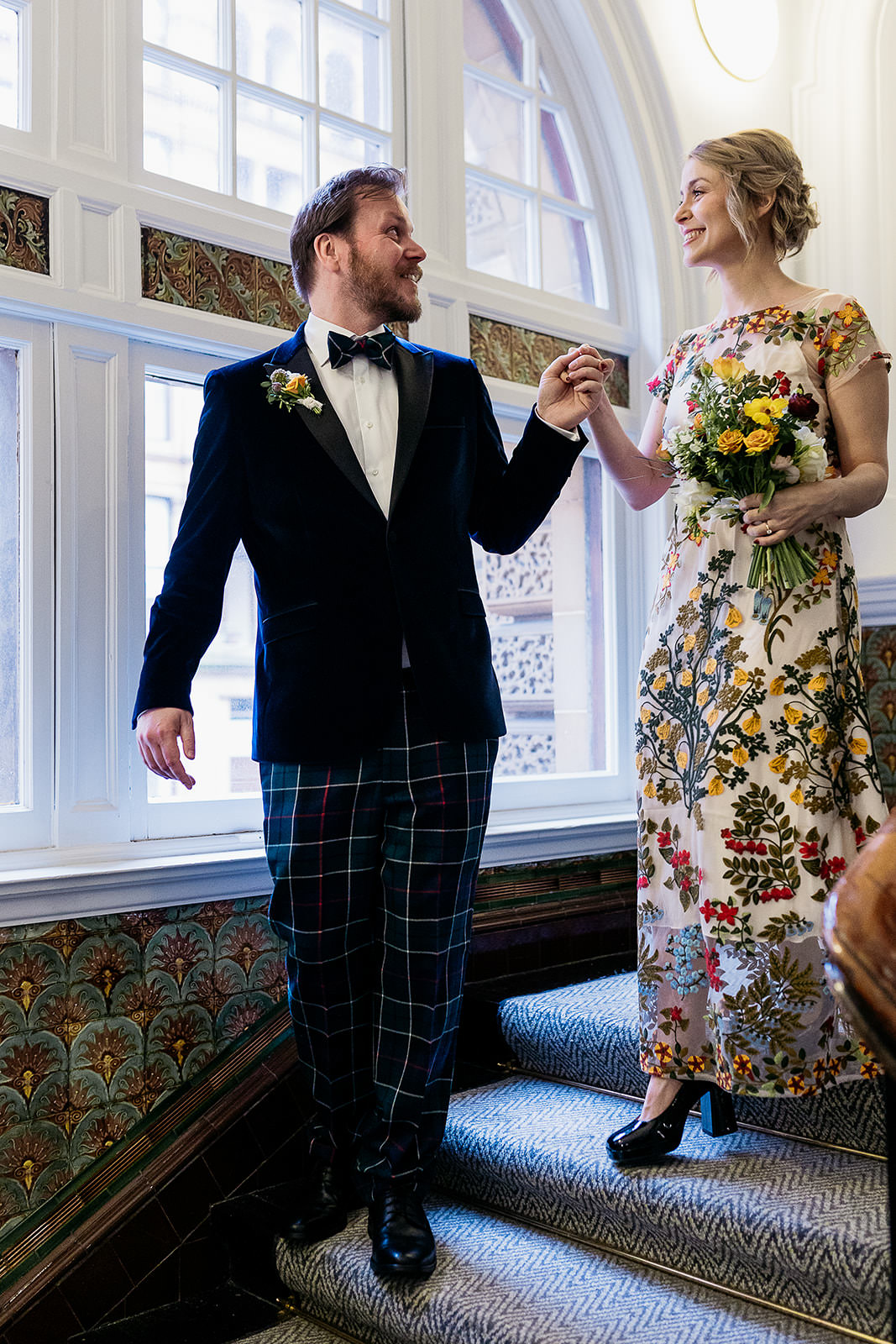 a groom is walking down the stairs in front of his wife and is holding her hand to lead her down.