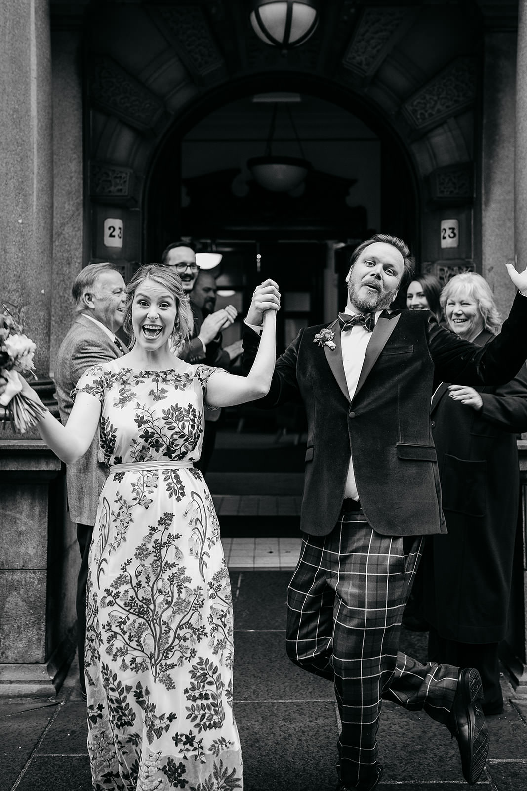 a bride and groom are walking out of the front door at montrose street at Glasgow city chambers. they are surrounded by their friends and family. they are all clapping and cheering.