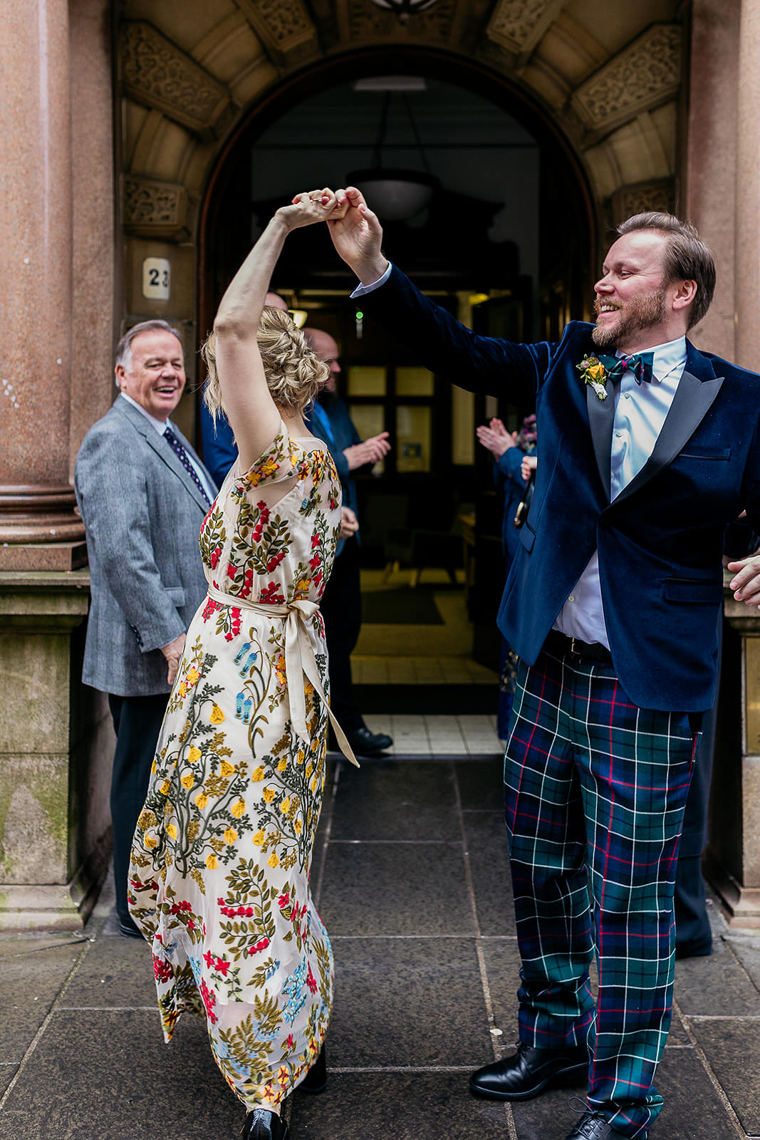 a bride and groom are walking out of the front door at montrose street at Glasgow city chambers. they are surrounded by their friends and family. they are all clapping and cheering.