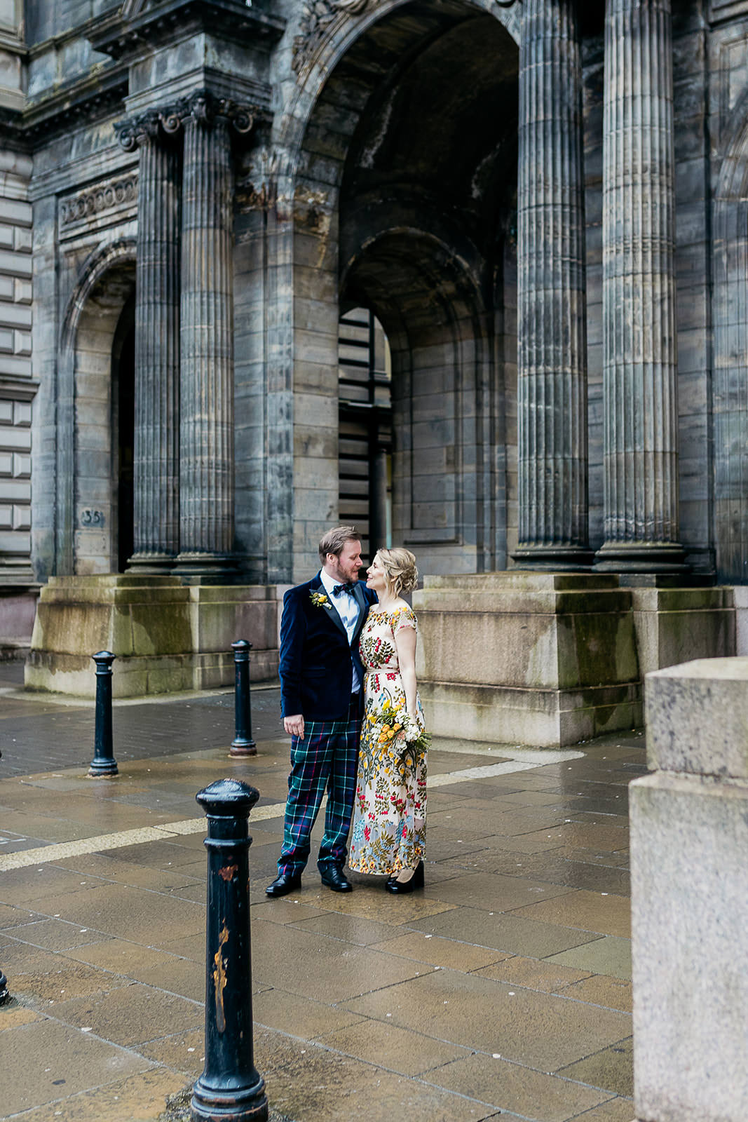 a bride and groom are standing side by side and holding each other close. they are standing in front of a set of stone arches.