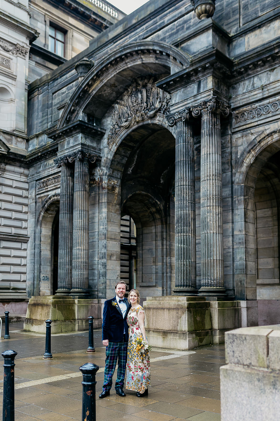 a bride and groom are standing side by side and holding each other close. they are standing in front of a set of stone arches.